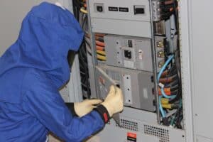 A person in a blue jacket and gloves works on a panel during arc flash safety training.