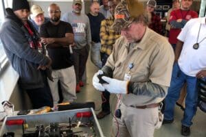 A man wearing a hat and gloves works on a device as part of his electrical safety training.