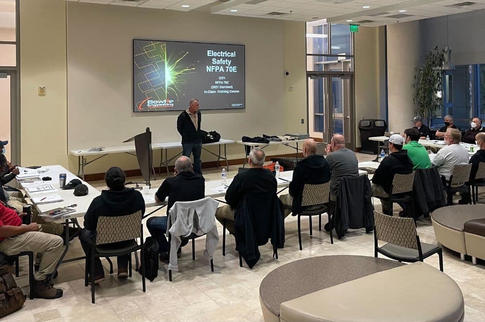 A man presents NFPA 70E training to an engaged audience of professionals in a conference room setting.