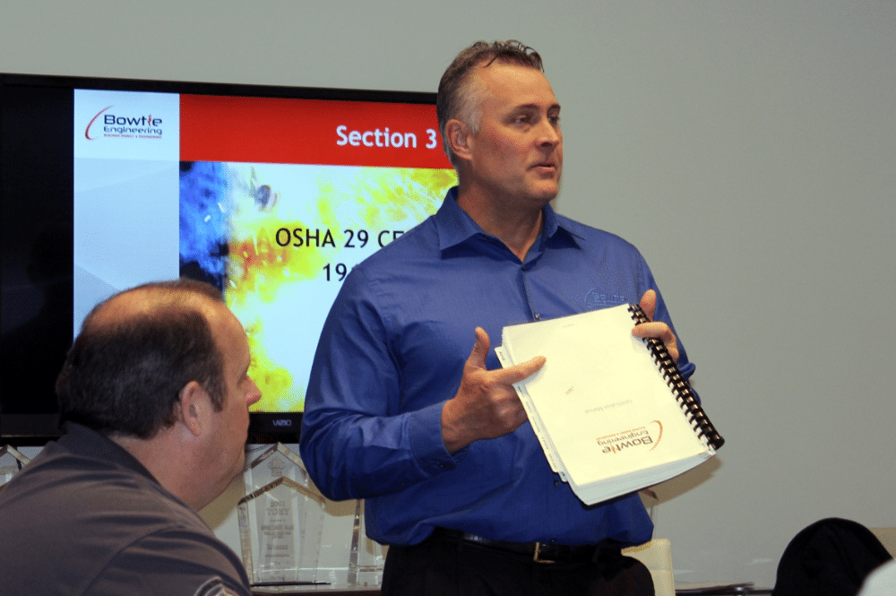 A man stand in front of engineers engaging in an Arc Flash assesment